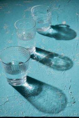 Mavi masada su olan üç bardağın yukarıdan görünüşü, gölgeler, dikey olarak, kopyalama alanı