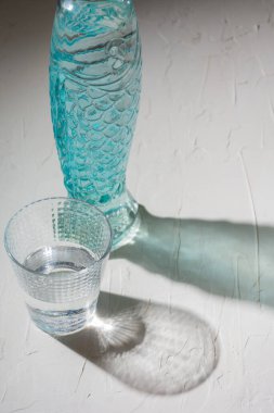 Bir bardak ve mavi bir şişe beyaz bir masanın üzerinde su, gölgeler, dikey, kopyalama alanı