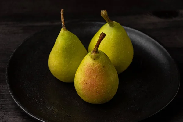 stock image Top view of three green pears with water drops in black plate on dark table, horizontal