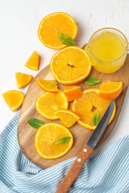 Portakal dilimlerinin yukarıdan görünüşü ve nane ve bıçak ile ahşap tahta, beyaz masa üzerinde mavi bez, dikey, kopyalama alanı ile