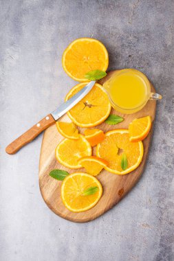 Dilimlerin üst görüntüsü, portakal, nane, tahta tahtada bıçak ve meyve suyu, gri arka plan, dikey, kopyalama alanı ile