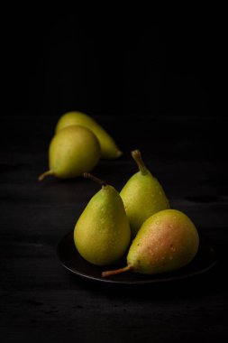 Siyah plakalı üç yeşil armudu kapat, arka planda iki tane daha, seçici odak, siyah arkaplan, dikey, kopyalama alanı