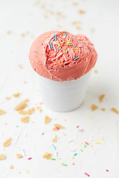 Beyaz kasedeki çilekli dondurmanın yukarıdan görünüşü beyaz masada, ekmek kırıntıları, dikey, fotokopi alanı ile.