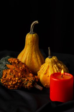 Masa örtüsü üzerinde turuncu mum olan üç balkabağının üst görünümü ve siyah arkaplan, dikey, kopyalama alanı ile