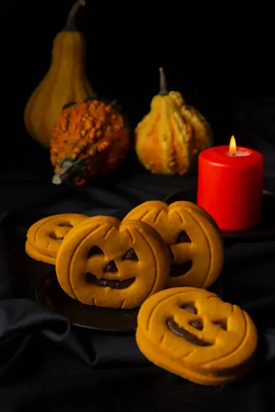 Close-up of pumpkin and chocolate cookies for Halloween on table with black tablecloth, candle and pumpkins, vertical, with copy space