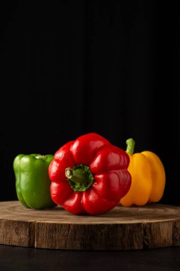 Ahşap ve koyu masa üzerinde yeşil, kırmızı ve sarı dolma biber manzarası, siyah arkaplan, dikey, kopyalama alanı ile