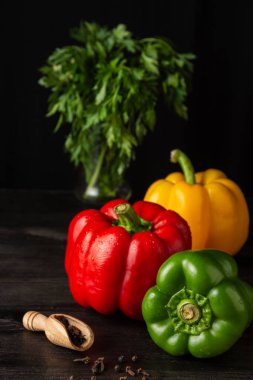 Arka planda baharatlar ve maydanozlu koyu ahşap masa üzerinde yeşil, kırmızı ve sarı dolma biber yakın plan, siyah arka plan, dikey, kopyalama alanı ile