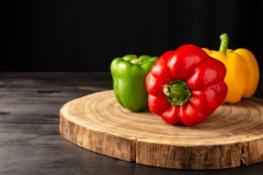 Ahşap ve koyu masa üzerindeki yeşil, kırmızı ve sarı dolma biber yakın plan, siyah arkaplan, yatay, kopyalama alanı olan