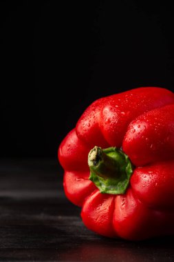 Koyu ahşap masa üzerinde su olan kırmızı biber yakın plan, siyah arkaplan, dikey, kopyalama alanı ile
