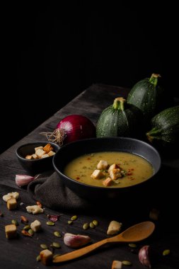 Üzerinde kabak çekirdeği, ekmek ve kırmızı biber bulunan ev yapımı kabak kremi, kumaş, sarımsak ve ahşap kaşık, siyah arka plan, dikey, fotokopi alanı olan koyu masa.