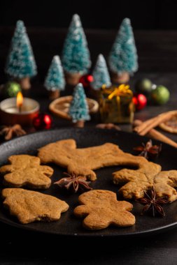 Tarçınlı zencefilli kurabiyeli tabağın üst görüntüsü, yıldız anason, portakal, Noel ağaçları ve mum, siyah arkaplan, dikey, kopyalama alanı ile