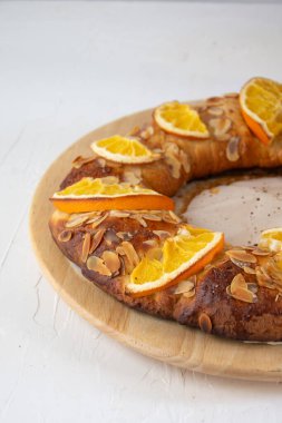 Yarı ev yapımı portakal ve bademli Roscon de Reyes manzarası, tahta tabakta, dikey, beyaz arka planda, tipik İspanyol Noel tatlısıyla, kopya alanı ile