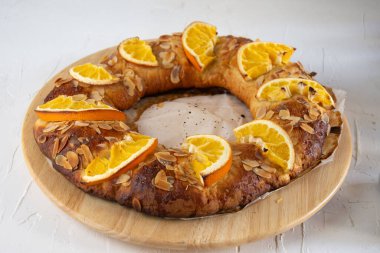 Portakal ve bademli ev yapımı Roscon de Reyes 'in ahşap tabakta, yatay, beyaz arka planda, tipik İspanyol Noel tatlısıyla fotokopi alanı.