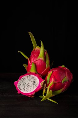 Üç pembe pitaya ya da ejderha meyvesi görüntüsü, biri açık, masa ve siyah arkaplan üzerinde, dikey, kopyalama alanı ile