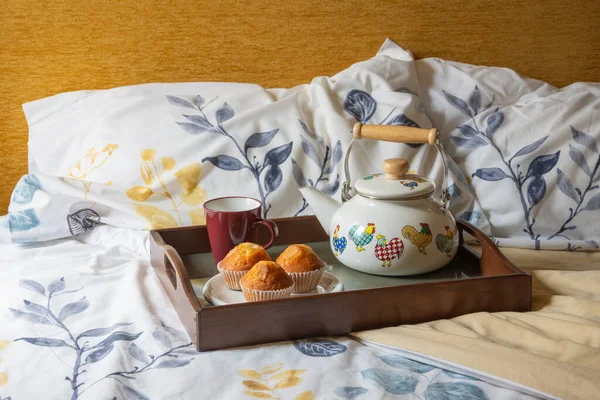 View of bed with sheets and pillows with breakfast tray with teapot and muffins, horizontal, with copy space