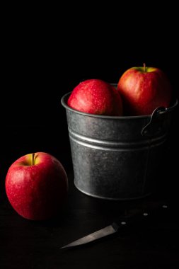 Elmalı ve bıçaklı kırmızı elmalı metal kovanın üst görüntüsü, siyah arka plan, dikey, kopyalama alanı olan.