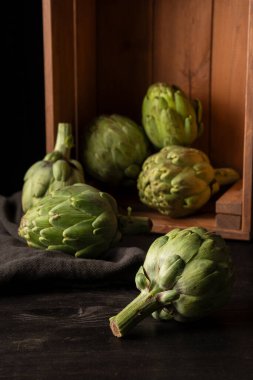 Kutudaki enginarların ve mutfak örtüsü, siyah arkaplan ve fotokopi alanı ile dikey koyu ahşap masanın yakınlaştırılması