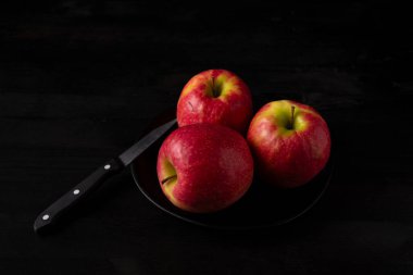 Tabakta üç kırmızı elmanın üst görüntüsü. Bıçak siyah masada, yatay ve kopyalama alanı var.