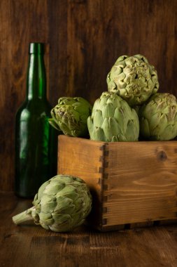 Masanın üzerinde enginarlar ve yeşil şişe olan tahta kutu görüntüsü ve tahta arka plan, dikey, kopyalama alanı olan