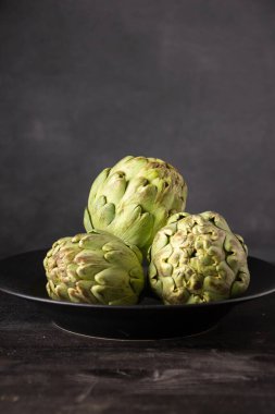 Seçici odaklı, koyu arkaplan, dikey, kopyalama alanı olan, tahta masadaki enginarların yakın plan görüntüsü