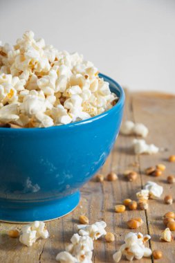 Kırsal ahşap masa üzerinde taze patlamış mısırla mavi kasenin üst görüntüsü, beyaz arka plan, kopyalama alanı ile dikey