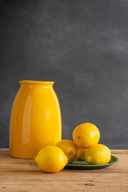 Yeşil plakalı, limonlu, koyu arkaplan, dikey, kopya alanı olan kırsal masa üzerindeki sarı vazo görüntüsü