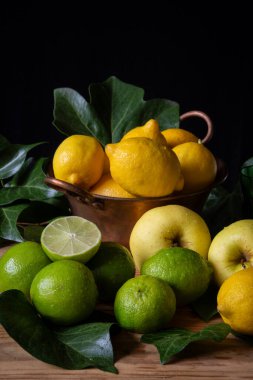 Sahneye limonlar, limonlar ve yeşil yapraklı sarı elmalarla yakın plan, dikey olarak siyah arkaplan, kopyalama alanı