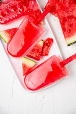 Karpuz parçalarıyla beyaz tabakta üç karpuz lolipopunun yukarıdan görünüşü, beyaz arka plan, dikey, kopyalama alanı ile