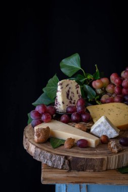 Peynirli kimyon, keçi peyniri, kırmızı üzüm, fındık, yeşil yaprak ve ekmek, siyah arka plan, dikey, fotokopi alanı olan bir köy masası.