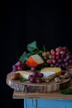 Peynir, kimyon, keçi peyniri, kırmızı üzüm, fındık ve ekmek, siyah arka plan, dikey, fotokopi alanı olan köy masası görüntüsü