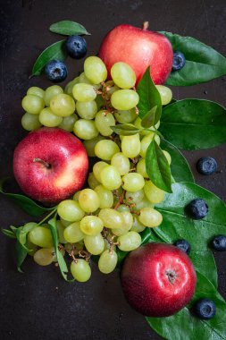 Üzüm, kırmızı elma ve yeşil yapraklı yaban mersini manzarası, koyu arka plan, dikey