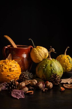 Sarı balkabağı, fındık, kaşık ve sonbahar yapraklı kil kap, siyah arkaplan, kopyalama alanı ile dikey