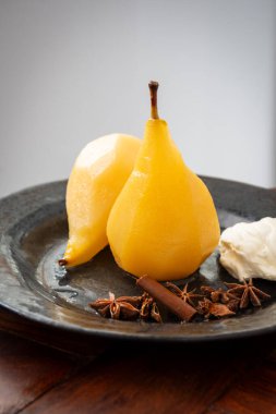 Anason, tarçın ve krema ile pişirilmiş iki armudun üst görüntüsü, koyu bir tabakta, beyaz arka plan, dikey, kopyalama alanı ile