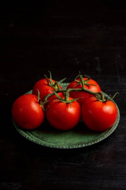 Yeşil tabakta ıslak domateslerin üst görüntüsü karanlık masada, kopyalama alanı ile dikey