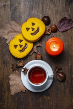 Cadılar Bayramı kurabiyeli bir fincan çayın üst görüntüsü, bir portakal mumu, yapraklar ve fındıklar, dikey olarak kopyalama alanı ile.