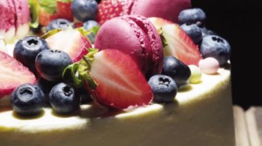 Siyah arka planda çilekli, yaban mersinli ve kurabiyeli beyaz çilekli pasta. makro video.