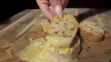 Uzun tırnaklı bir kız bir parça ekmeği erimiş Camembert peynirine batırıyor.