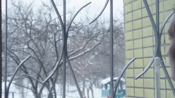 那女孩站在雪地上用栅栏向窗外望去 — 图库视频影像