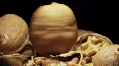 Siyah arka planda kırılmış bir ceviz, diğer cevizlerle birlikte bir yığın içinde hızla döner ve durur. Yakın plan..