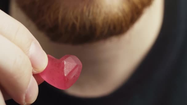 Jovem Com Casaco Preto Barba Vermelha Comendo Goma Forma Coração — Vídeo de Stock