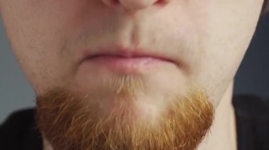 Siyah ceketli, kırmızı sakallı, kırmızı kalp şeklinde jelibon yiyen genç bir adam.