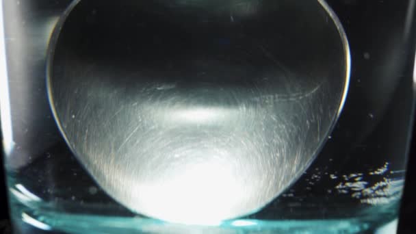 玻璃杯中的勺子 黑色底座上有水 特写滑梯 — 图库视频影像