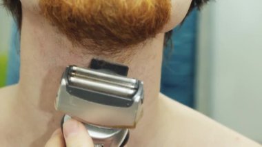 Kızıl sakallı, elektrikli tıraş makinesi olan genç bir adamın traş süreci..