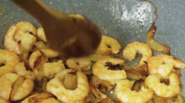 Karidesler kızartma tavasına konur yağda kızartılmış soğan, kaşıkla karıştırılır, yakın plan.