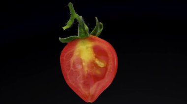 Yeşil yapraklı küçük dilimlenmiş domates, döner. Siyah bir arkaplanda yakın plan.