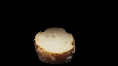 Rotating piece of baguette on a black background. Close-up.