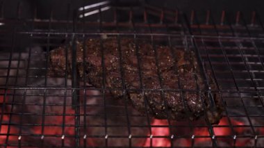Ribeye steak on a wire rack. Hot coals, fat dripping from the meat. Close-up.