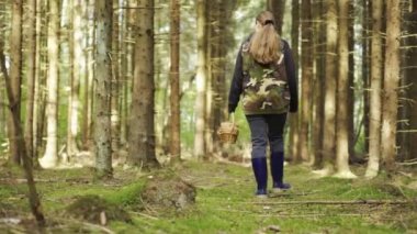 A girl in a camouflage jacket walks through the woods with a basket. Looking for mushrooms.