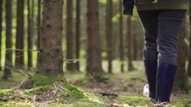 A girl in blue boots with a basket is looking for mushrooms. Close-up. The pursuit.