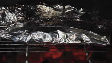 Flatbreads wrapped in foil, cooking on coals. Grill close-up.